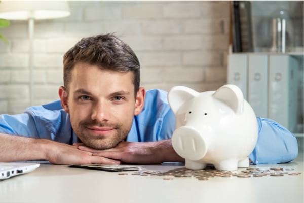 Adult male smiling next to piggybank
